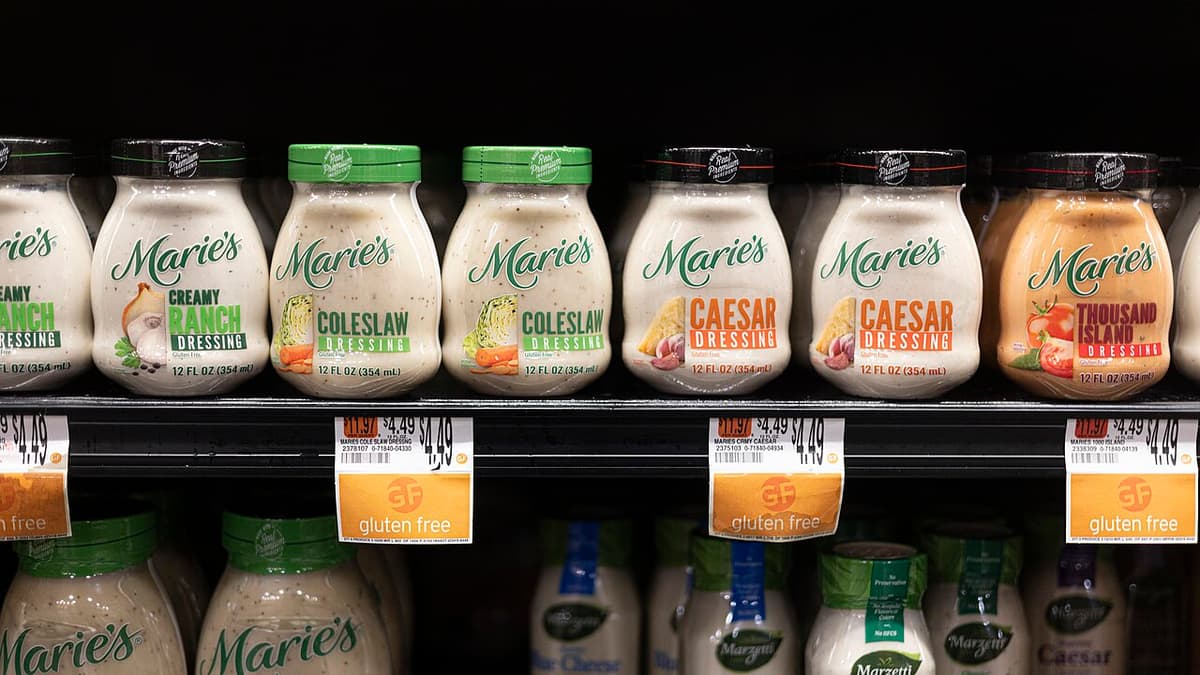 Salad dressing jars on a supermarket shelf above printed price labels